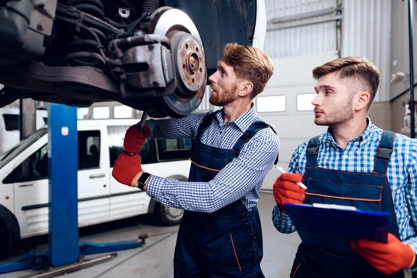 Vader en zoon werken op de auto-service. Twee monteurs werken met de gegevens van de auto. — Stockfoto