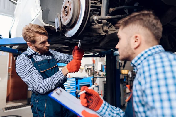 Padre e hijo trabajan en el servicio de autos. Dos mecánicos trabajan con los detalles del coche . — Foto de Stock