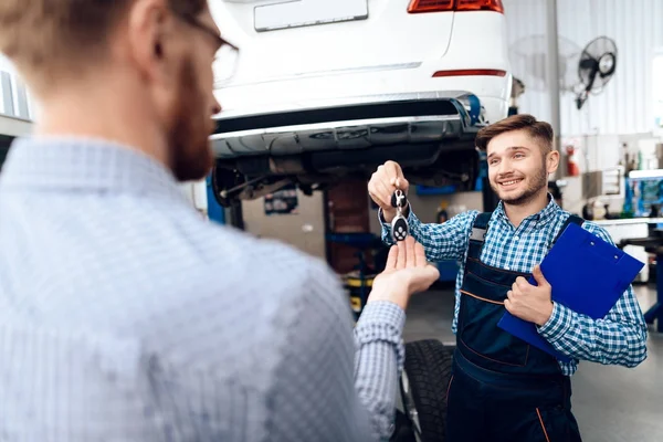 Mannen tar sin bil från tjänsten auto. Mekanikern överför bilnycklarna till kunden — Stockfoto