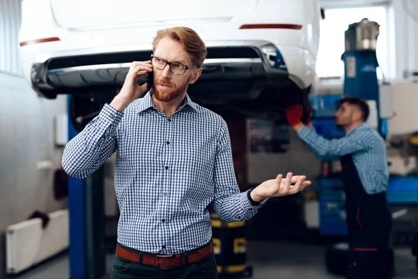 The mechanic repairs the car while the customer is talking on the phone.