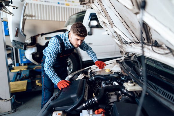 A young man works at a service station. The mechanic is engaged in repairing the car.