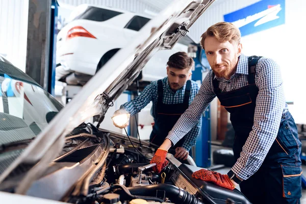 Padre e hijo trabajan en el servicio de autos. Dos mecánicos trabajan con los detalles del coche . — Foto de Stock