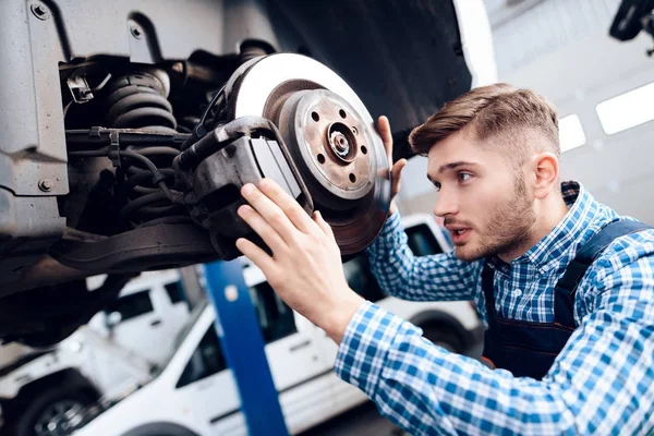 若い男は、サービス ステーションで動作します。メカニックが車の修理に従事しています。. — ストック写真