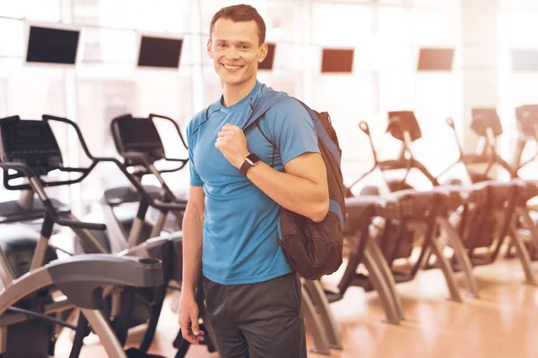 Un joven está posando en el gimnasio. Un hombre musculoso con una camiseta azul sonríe . — Foto de Stock