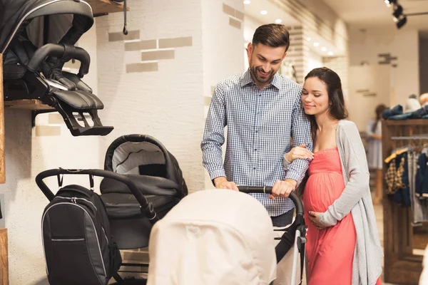 Una mujer embarazada junto con un hombre eligen un carro de bebé . — Foto de Stock