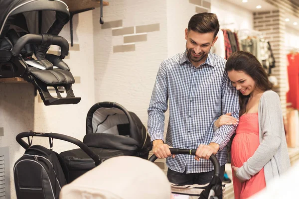 Una mujer embarazada junto con un hombre eligen un carro de bebé . — Foto de Stock