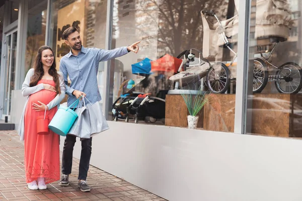 Una mujer embarazada con un hombre caminando por el escaparate con artículos para niños . — Foto de Stock