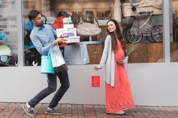 Беременная женщина с мужчиной, проходящим мимо витрины магазина с детским товаром
.