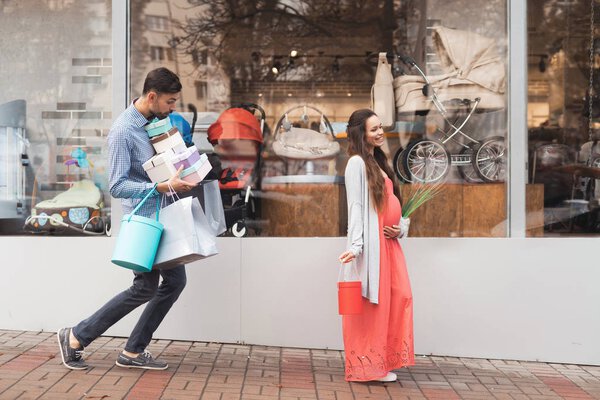 Беременная женщина с мужчиной, проходящим мимо витрины магазина с детским товаром
.