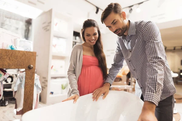 Una mujer embarazada con un hombre elige un baño de bebé en una tienda . — Foto de Stock