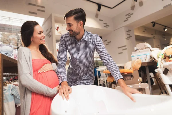 Eine schwangere Frau mit einem Mann wählt ein Babybad in einem Geschäft. — Stockfoto