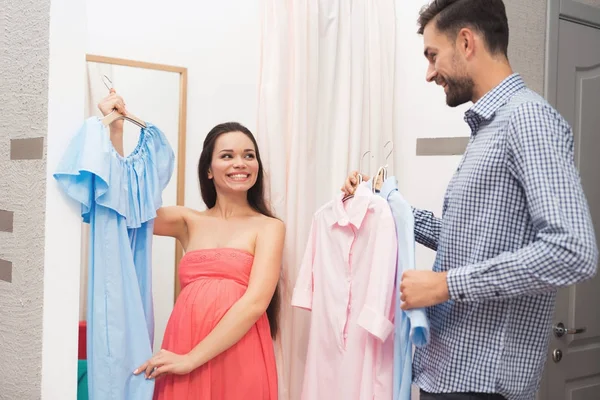 Una mujer embarazada con un hombre elige vestidos en la tienda . — Foto de Stock