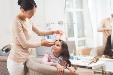 Kuaför saç şekillendirme için küçük bir esmer kızın işi. Kız Güzellik Salonu sandalyede oturuyor.