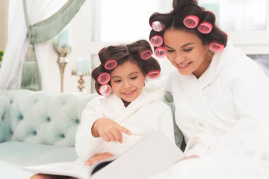 Anne ve kızı beyaz bornoz içinde kanepede oturuyorsun. Onlar-si olmak curlers saçlarını.