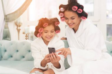 Anne ve kızı beyaz bornoz içinde kanepede oturuyorsun. Onlar-si olmak curlers saçlarını.