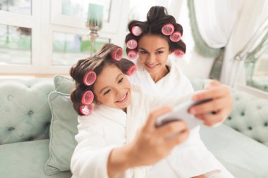 Anne ve kızı beyaz bornoz içinde kanepede oturuyorsun. Onlar-si olmak curlers saçlarını.