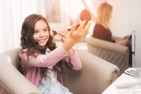 Menina bonita no salão de beleza. A rapariga faz uma maquilhagem. Ela sorri e gosta de se parecer com sua mãe . — Fotografia de Stock