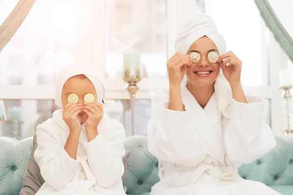 Foto de madre e hija en batas blancas. Se ponen trozos de pepino en los ojos. . —  Fotos de Stock