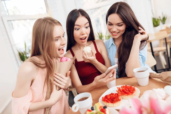 Tres chicas miran a la pantalla del teléfono inteligente, celebrando la fiesta el 8 de marzo . —  Fotos de Stock