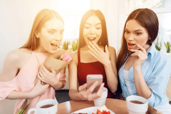 Tres chicas miran a la pantalla del teléfono inteligente, celebrando la fiesta el 8 de marzo . — Foto de Stock