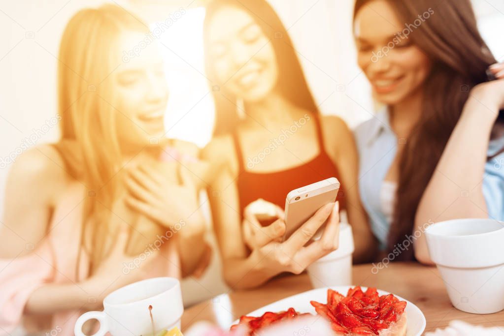 Three girls look at the smartphone screen, celebrating the holiday on March 8.