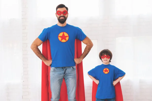 Padre e hijo con los trajes rojos y azules de superhéroes. En sus rostros hay máscaras y están en impermeables. . — Foto de Stock