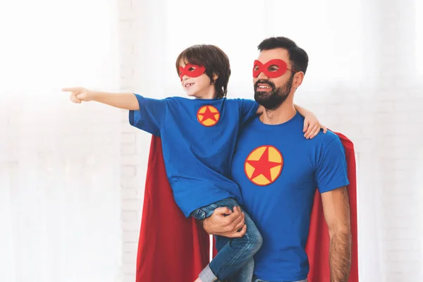 Vater und Sohn in den rot-blauen Anzügen der Superhelden. auf ihren Gesichtern sind Masken und sie tragen Regenmäntel. — Stockfoto
