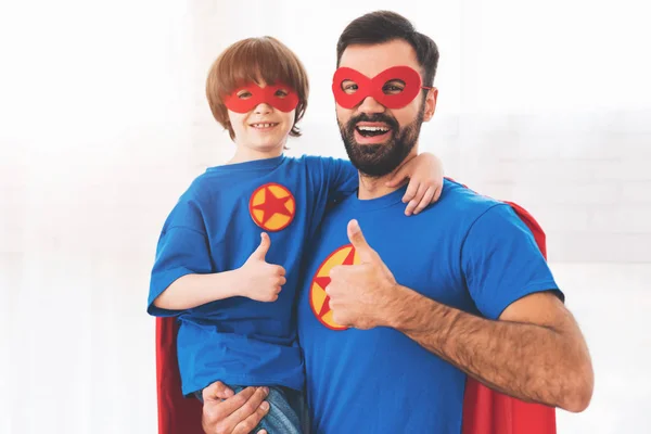 Father and son in the red and blue suits of superheroes. On their faces are masks and they are in raincoats.