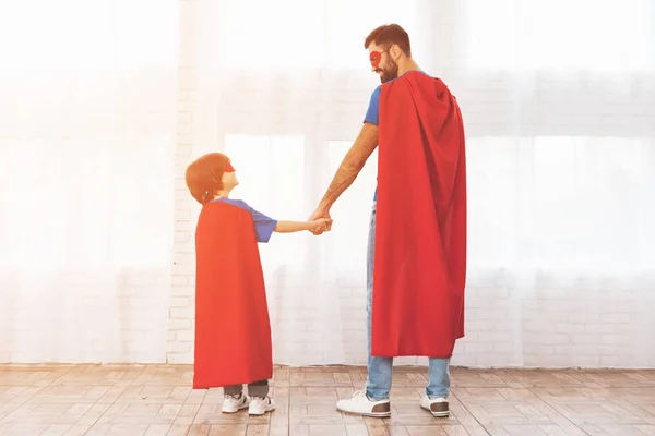 Padre e hijo con los trajes rojos y azules de superhéroes. En sus rostros hay máscaras y están en impermeables. . — Foto de Stock