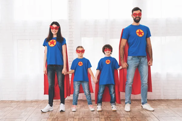 Junge Familie in roten und blauen Anzügen von Superhelden. ihre Gesichter in Masken und sie sind in Regenmänteln. — Stockfoto