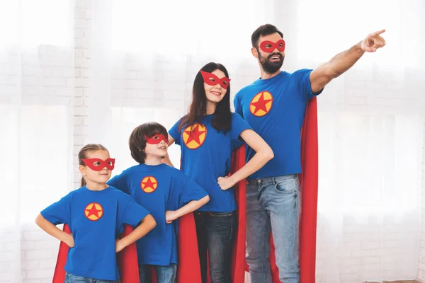 Familia joven en trajes rojos y azules de superhéroes. Sus rostros en máscaras y están en impermeables . — Foto de Stock