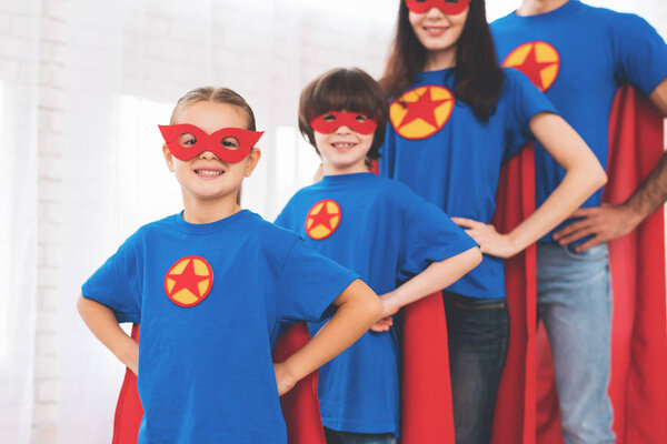 Young family in red and blue suits of superheroes. Their faces in masks and they are in raincoats.