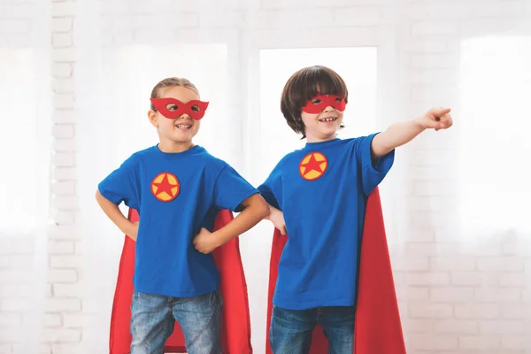 Niños con trajes rojos y azules de superhéroes. Llevan máscaras. Niños posando en habitación luminosa . — Foto de Stock