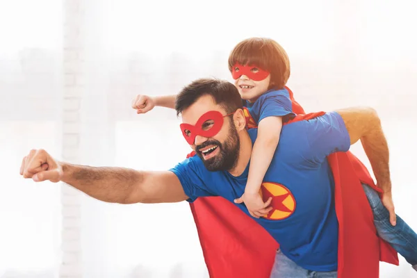 Vater und Sohn in den rot-blauen Anzügen der Superhelden. auf ihren Gesichtern sind Masken und sie tragen Regenmäntel. — Stockfoto