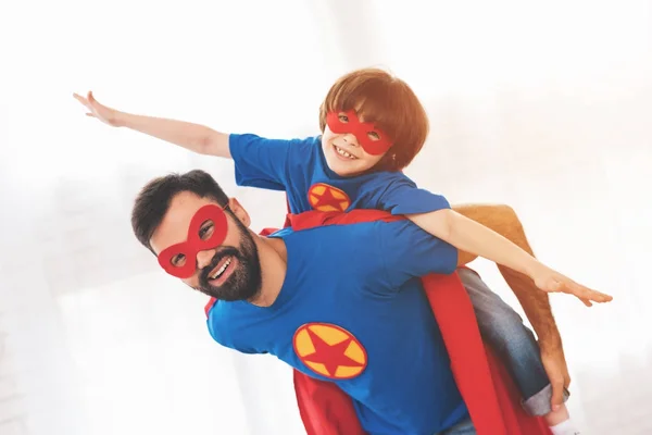 Otec a syn v červené a modré obleky, superhrdinové. Na jejich obličeje jsou masky a jsou v pláštěnky. — Stock fotografie