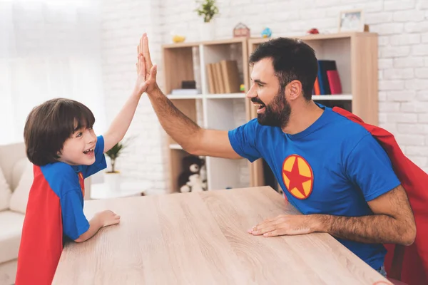 Father and son in suits of superheroes. They compete in arm-wrestling.