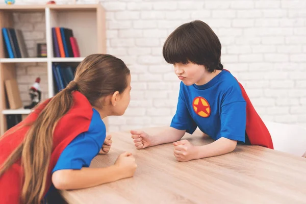 Una niña y un niño con trajes de superhéroes. Ellos miden su fuerza en una habitación luminosa — Foto de Stock