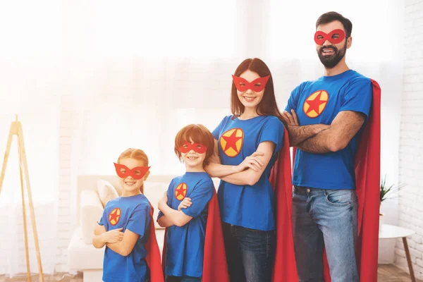 Familia joven en trajes rojos y azules de superhéroes. Sus rostros en máscaras y están en impermeables . — Foto de Stock