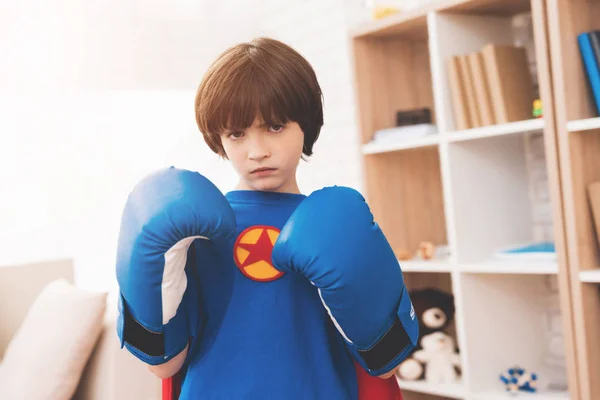 Un niño moreno con una camisa de superhéroe. Él posa con guantes de boxeo. — Foto de Stock
