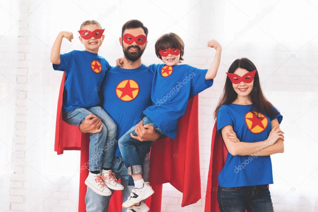 Young family in red and blue suits of superheroes. Their faces in masks and they are in raincoats.