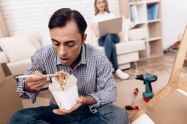 Man handyman is engaged in the assembly of furniture. He eats Chinese noodles during working break. — Stock Photo, Image
