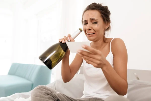 Eine einsame Frau weint allein, ihre Wimperntusche ist geflossen. sie sitzt auf einem Bett in einem hellen Zimmer. — Stockfoto