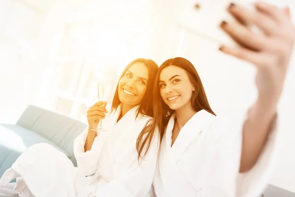 Mädchen amüsieren sich bei der Polterparty. Brünetten in weißen Bademänteln haben Spaß in einem hellen Raum. — Stockfoto