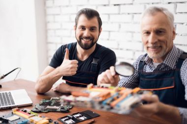 Yaşlı ve genç erkekler birlikte bir büyüteç ile bilgisayardan parçası bakmak.