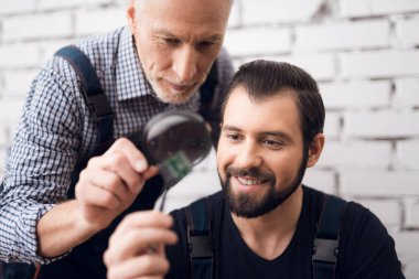 Yaşlı ve genç erkekler birlikte bir büyüteç ile bilgisayardan parçası bakmak.