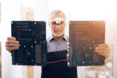 Bir yaşlı bilgisayar onarım uzmanına bir anakart ile bir kamera için poz.