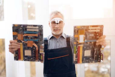 Bir yaşlı bilgisayar onarım uzmanına bir anakart ile bir kamera için poz.