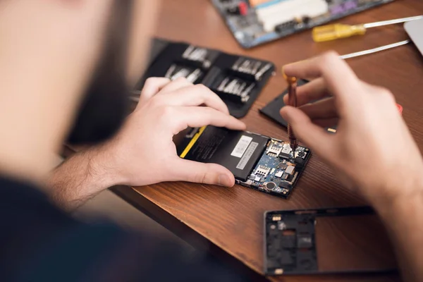 Un hombre está reparando un teléfono móvil. En el marco, sus manos y detalles del dispositivo . — Foto de Stock