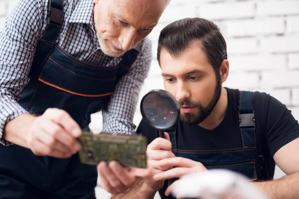 Alte und junge Männer betrachten gemeinsam das Teil vom Computer aus durch eine Lupe.. — Stockfoto