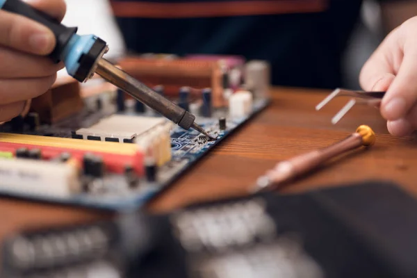 A man with a soldering iron repairs computer equipment.